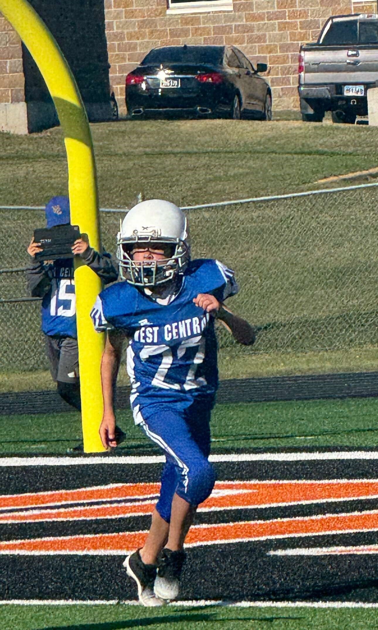 Youth football player in a blue and white West Central jersey with the number 22 running across an end zone line during a outdoor game.