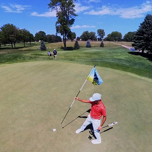 An image that's looking down on a golfer placing a flag back in the hole on the putting green.